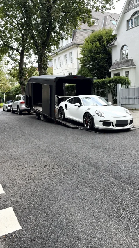 Porsche blanche et remorque fermée dans une rue arborée